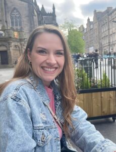 Photo of a woman with blond hair smiling at the camera wearing a denim jacket and pink shirt.